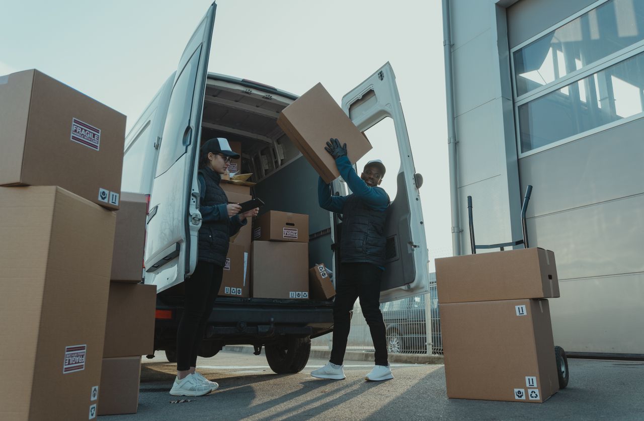 services-01 Workers loading boxes into a delivery van at a warehouse facility outdoors.