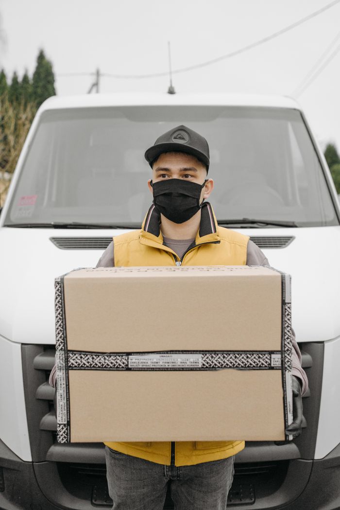 gallery-5 A delivery worker wearing a mask holds a large package in front of a van.