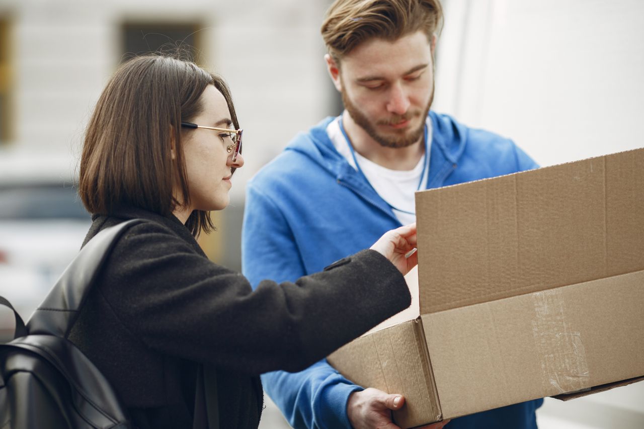 gallery-2 Man and woman handling a package outdoors. Urban delivery scene with cardboard box.