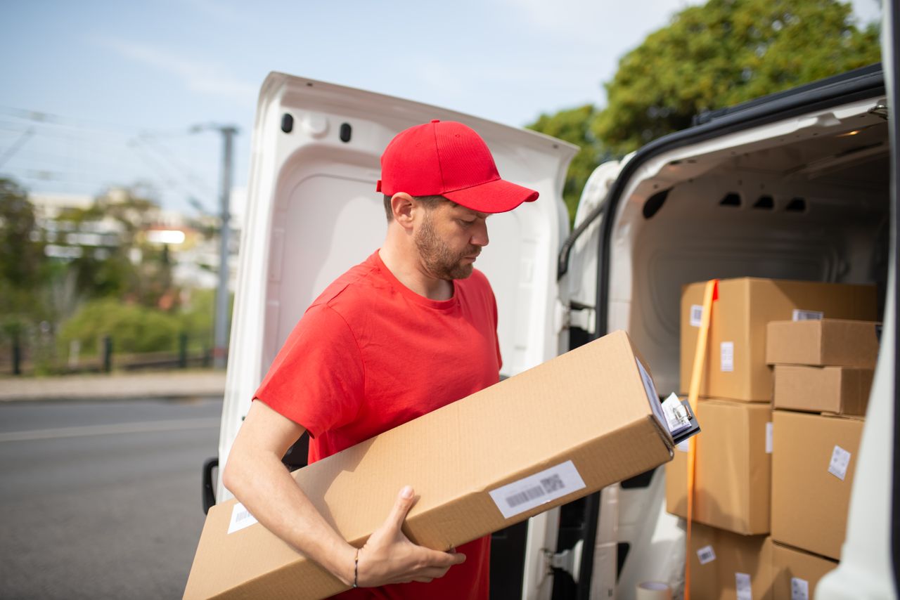 gallery-4 Courier in red uniform unloading packages from a delivery van on a sunny day.
